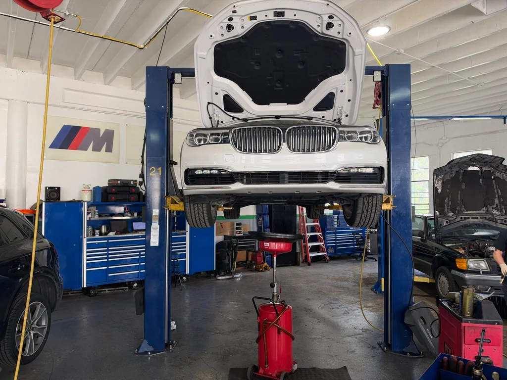 A white BMW on a blue lift with its hood open inside the 4 Rings workshop